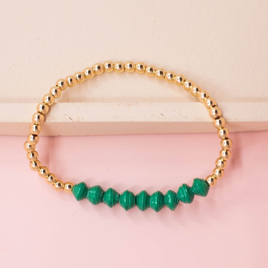 stackable bracelet made of 14k gold plated brass beads and handmade paper beads. The brass beads are round and shiny, while the paper beads are colorful and textured, creating a striking contrast. The bracelet is designed to be worn with other bracelets and features an elastic band that fits most wrist sizes. It is displayed on a neutral background with good lighting that highlights the details and craftsmanship of the bracelet.