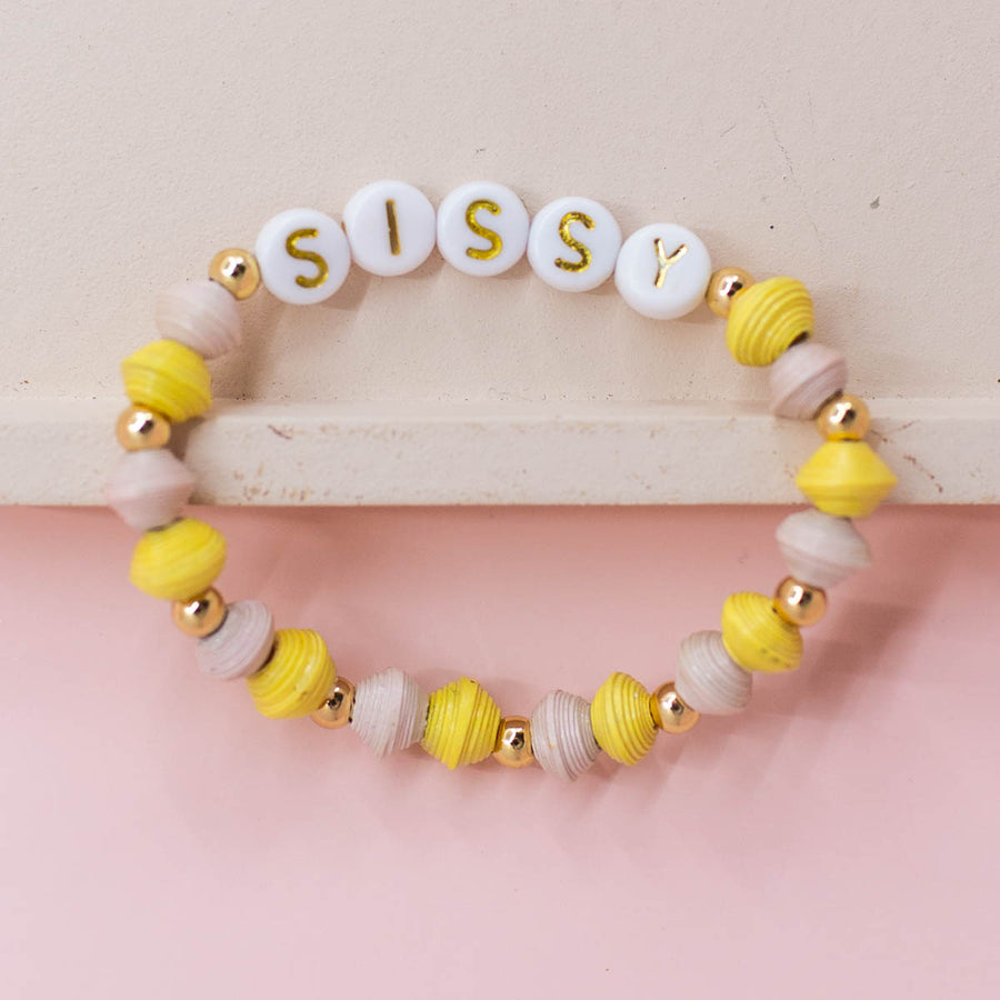 Ethically made fair trade bracelet with handmade paper beads and gold letter beads spelling sissy