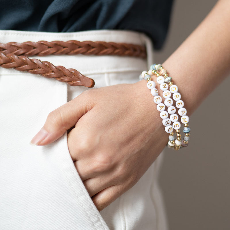 Woman wearing a stack of letter bead bracelets with three words dream inspire breathe close up