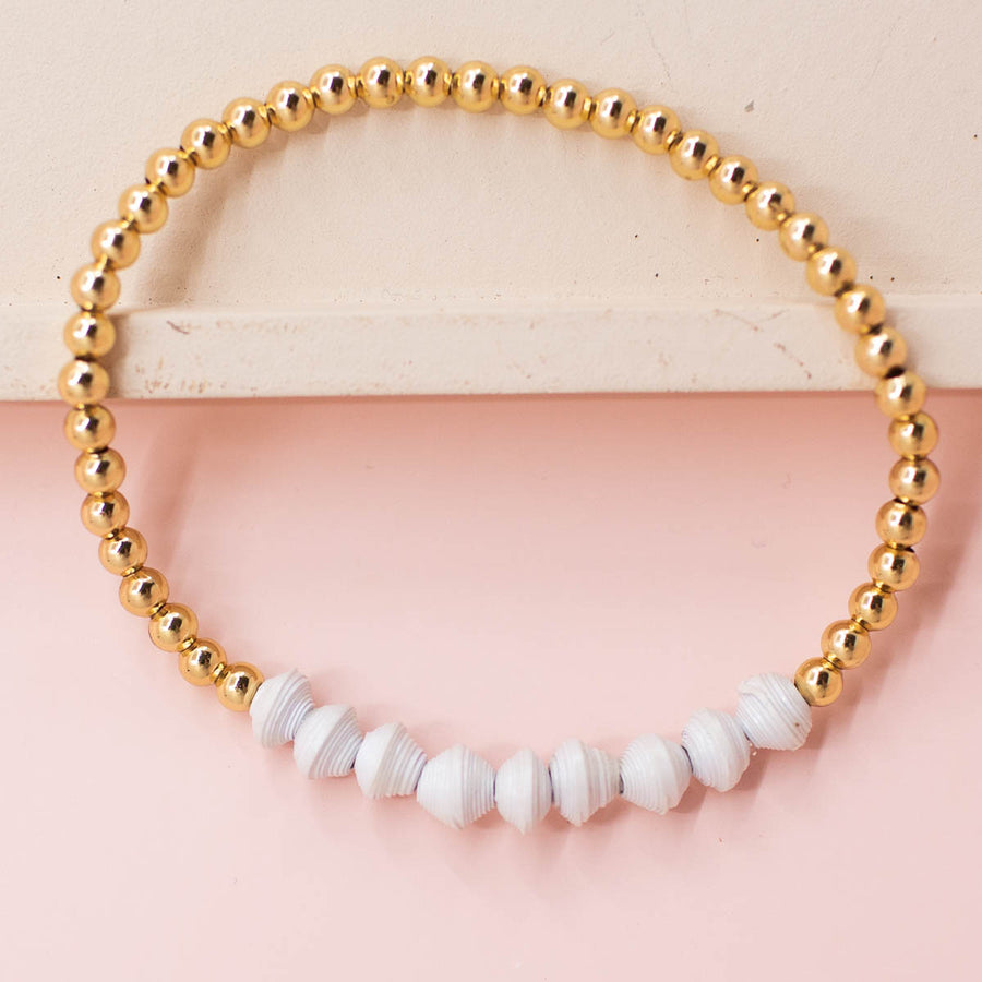 stackable bracelet made of 14k gold plated brass beads and handmade paper beads. The brass beads are round and shiny, while the paper beads are colorful and textured, creating a striking contrast. The bracelet is designed to be worn with other bracelets and features an elastic band that fits most wrist sizes. It is displayed on a neutral background with good lighting that highlights the details and craftsmanship of the bracelet.